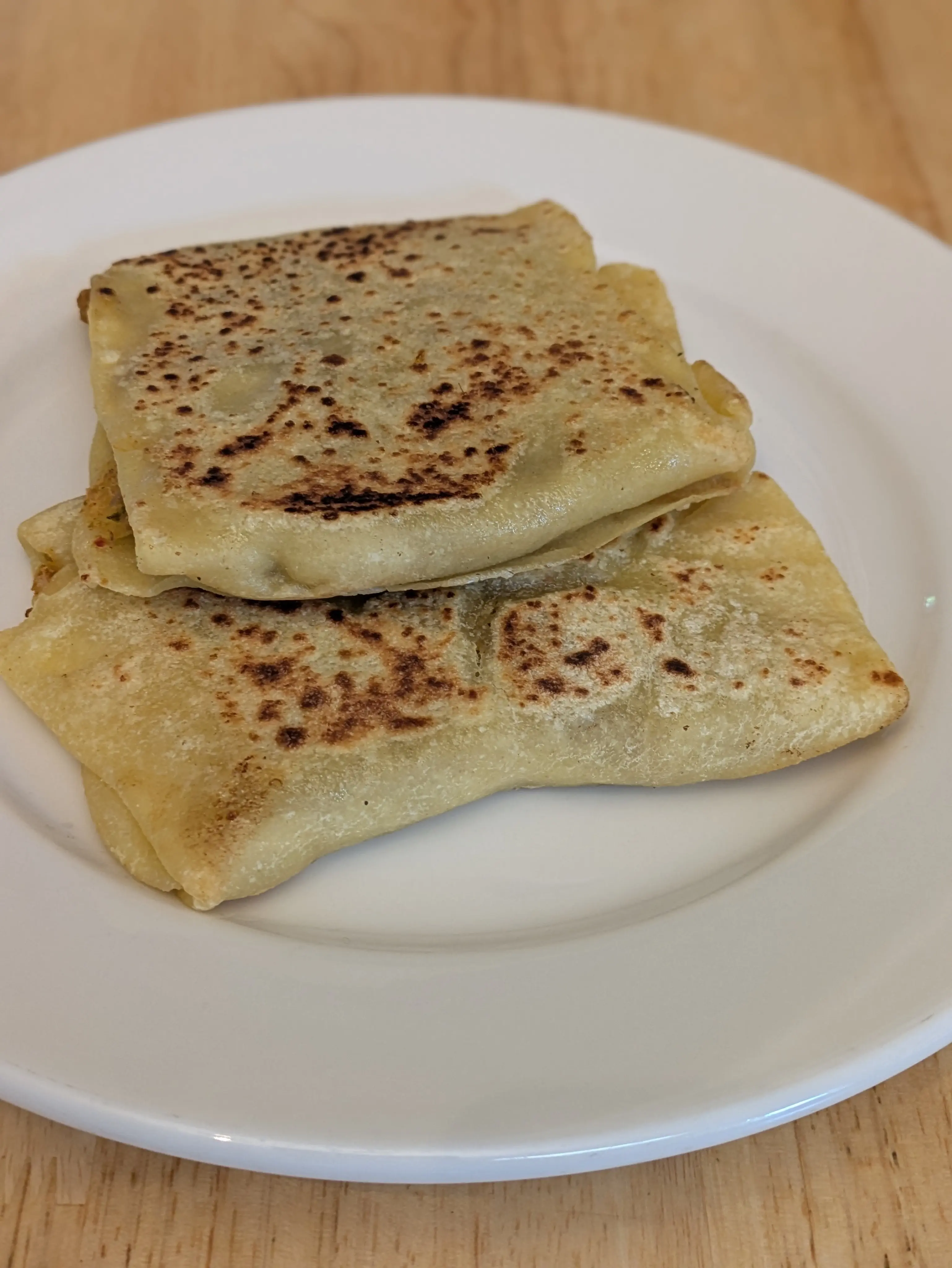 two semolina flour based stuffed flatbreads in a square or rectangular shape sitting on a white plate.